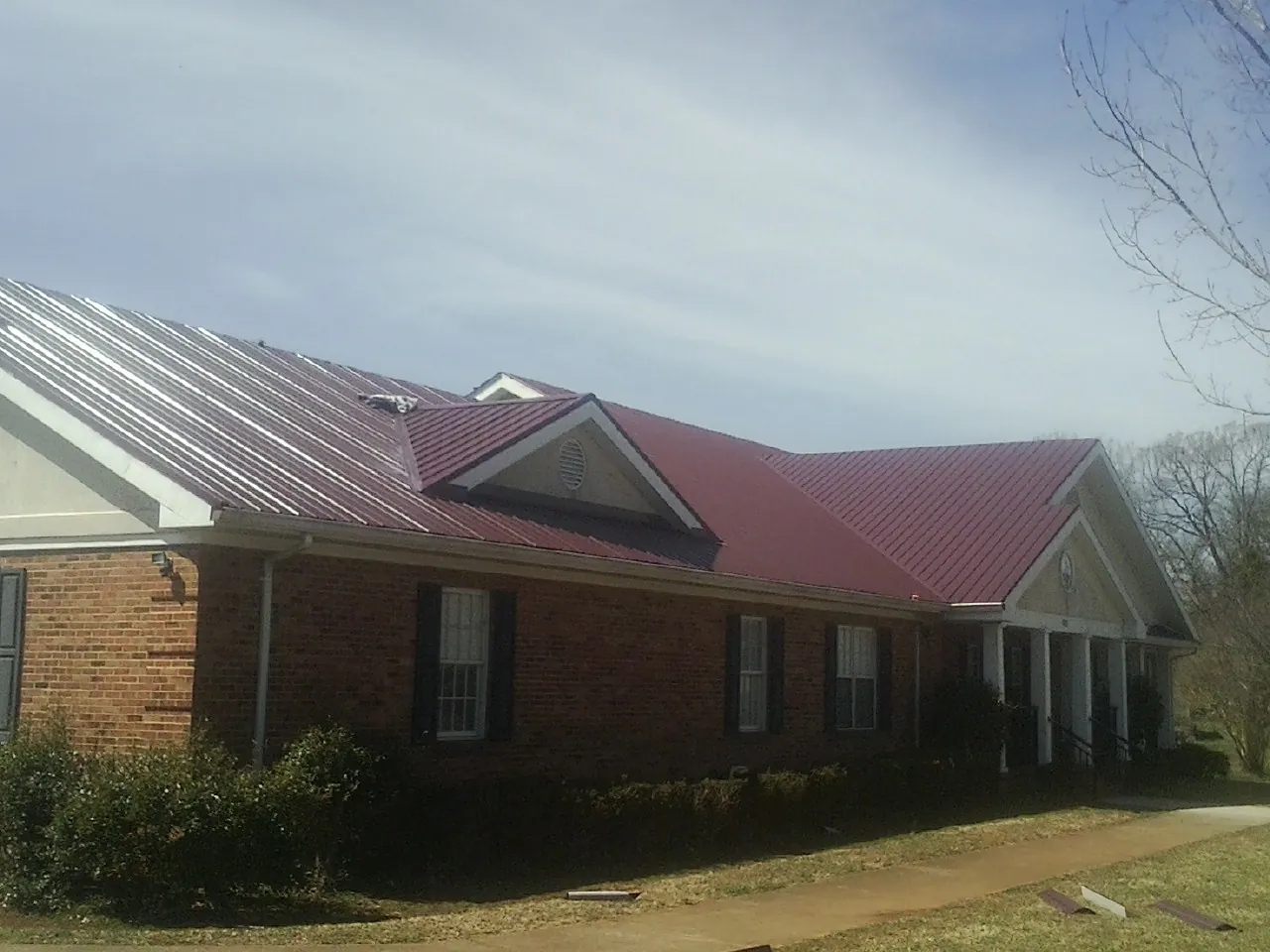 Red metal roof with gabled entries on a long brick building, from a Hail Damage Roof Repair job in Doylesburg