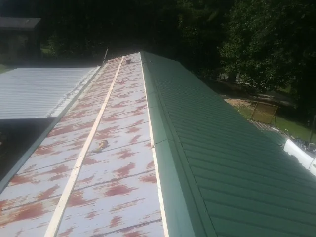 Old rusted panels beside newly installed green metal roofing — Wind Damage Roof Repair by Roofing Brothers in Doylesburg