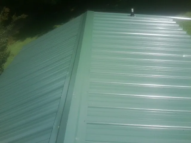 New green metal panels meeting at the ridge of a roof — Flat Roof Repair work by our crew in Doylesburg
