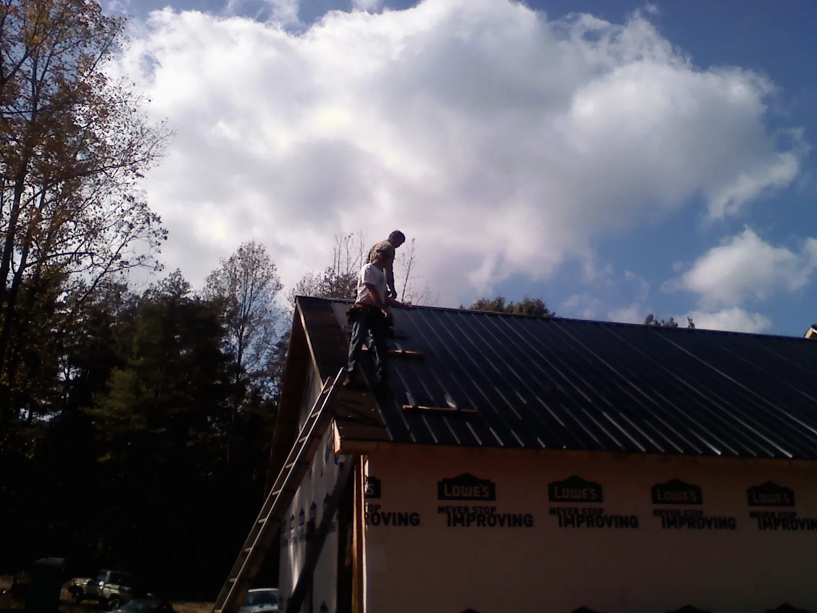 Roofer fastening dark metal panels high against a cloudy sky, from a Roof Inspection job in Doylesburg