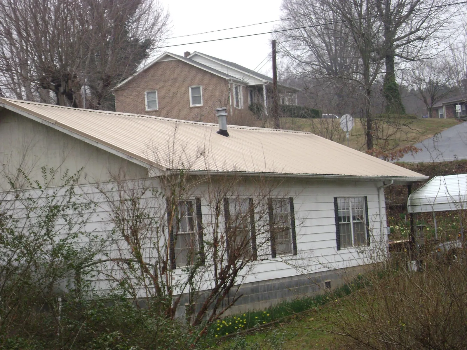 Tan metal roof on a white sided house set into a hillside — Commercial Roofing by Roofing Brothers in Doylesburg